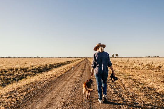 Woman photographer holding camera walking away along road with dog