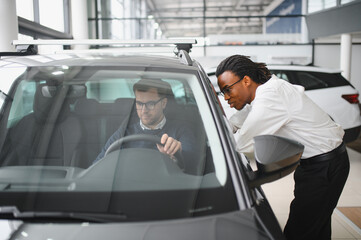 Male car dealer helps customer choose car in car dealership. Man buys new car