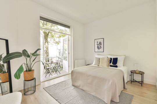 A stylish modern bedroom featuring a cozy bed, contemporary decor, and large windows opening to a balcony. It showcases minimalist design elements and neutral tones.