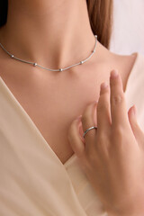 Cropped image of young woman wearing delicate silver necklace with small spherical accents and a simple ring. Concept of jewelry, luxury, accessories, beauty