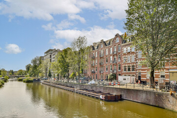 A picturesque view of a canal lined with trees and historic buildings, showcasing a vibrant urban landscape with boats and clear blue skies.