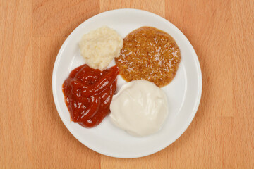 A white plate holds four distinct condiments: horseradish, ketchup, mayonnaise, and mustard