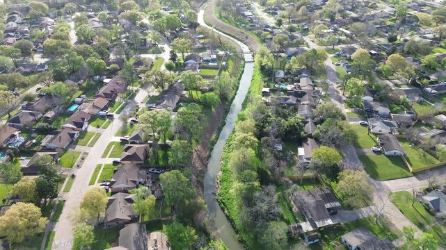 S curved Cole Creek grass-lined channel river along Langfield Road in Fairbanks Northwest Crossing neighborhood, Harris County, greater Houston area, early morning spring, suburban detached homes
