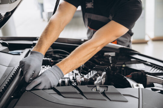 Close-up shot of unrecognisable man wearing gray glove inspecting car engine and interior of hood of car