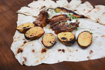 Grilled lamb ribs with grilled potatoes and herbs on pita bread. Pork barbecue. Potato bbq. Fried lamb on a table. Fast food. Restaurant food