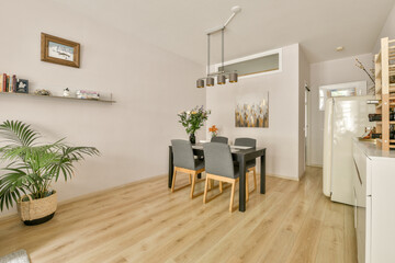 A contemporary dining area featuring a sleek table and chairs, complemented by greenery and soft wooden flooring, creating a warm and inviting ambiance.