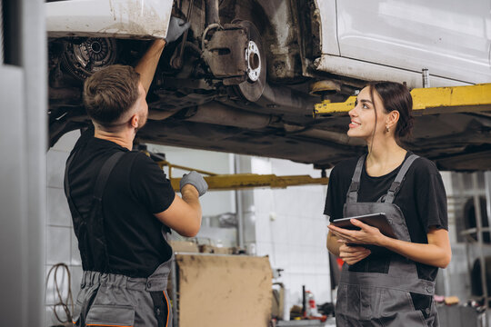 Young expert female inspects repair checklist with automotive mechanic worker partner, quality suspension technician team at fix garage. Vehicle maintenance service works industry occupation job. - Powered by Adobe