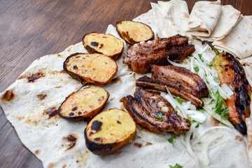 Grilled lamb ribs with grilled potatoes and herbs on pita bread. Pork barbecue. Potato bbq. Fried lamb on a table. Fast food. Restaurant food