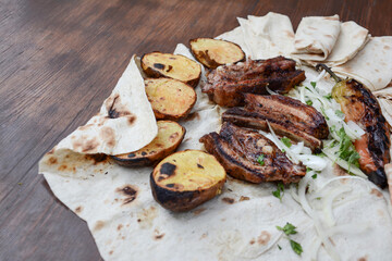 Grilled lamb ribs with grilled potatoes and herbs on pita bread. Pork barbecue. Potato bbq. Fried lamb on a table. Fast food. Restaurant food