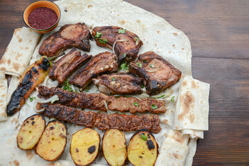 Barbecue with grilled meat and shish kebab. Grilled lamb ribs, kebab, potatoes and pita bread on wooden board. Restaurant food, pork barbecue, bbq.