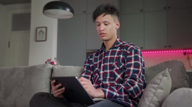 focused creative man drawing on tablet with stylus at home. digital designer, illustrator, or architect working on cozy sofa in stylish apartment