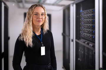 Female IT professional in datacenter with confident expression wearing security identification...