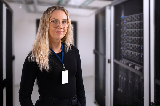 Female IT professional in datacenter with confident expression wearing security identification badge. IT consultant in server and network room