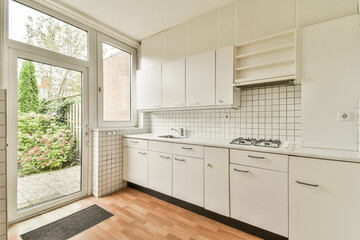 A sleek, modern kitchen featuring white cabinets and a view of a lush garden through large windows, blending indoor comfort with outdoor beauty.