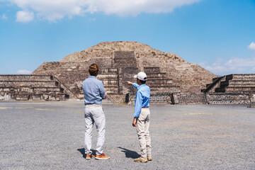 Two men stand in front of the Pyramid of the Moon in Teotihuacán, Mexico, with one gesturing...