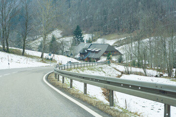 Obraz premium Winding road leads through tranquil snowy landscape towards a cozy cabin nestled in the mountains during a quiet winter day