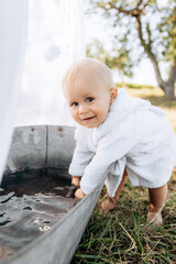 Little boy in a white coat near a bathtub with water in the garden on the grass