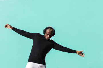Young African man isolated on blue background listening music and dancing