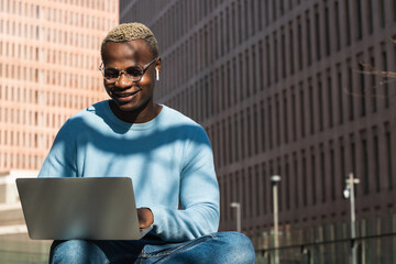 African american male student using laptop and learning online, doing homework outdoors in university campus park