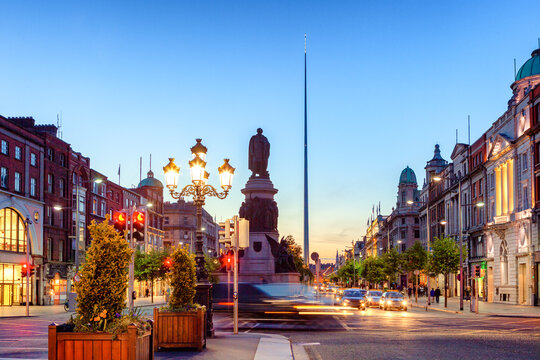 O Connell Street in Dublin, Ireland, with historic buildings, the Spire of Dublin, and blurred motion vehicles.