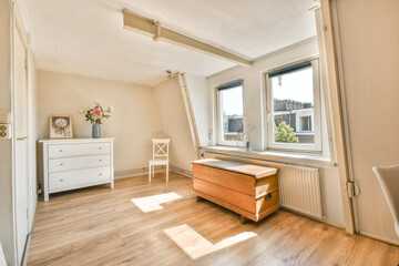 A sunny minimalist interior featuring wooden flooring, white furniture, and natural light streaming through large windows, creating a warm and inviting atmosphere.