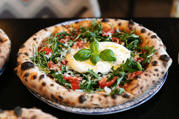 Neapolitan pizza with burrata, arugula, cherry tomatoes, and fresh basil