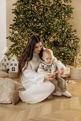 Mother and son sitting near a Christmas tree with a garland before the New Year and Christmas