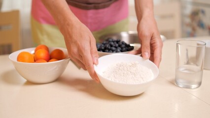 Woman holding bowl of flour with apricots and blueberries in background