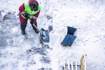 Snowy city: a snow cleaner in a bright vest shovels loose snow from the pedestrian area during...