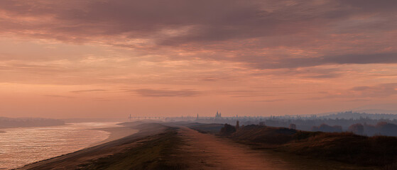 Fototapeta premium A beautiful sunset over a beach with a city in the distance