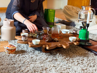 A woman pours yellow tea during a traditional gongfu tea ceremony on a carved wooden tray. Ritual, attention and mindfulness through tea preparation