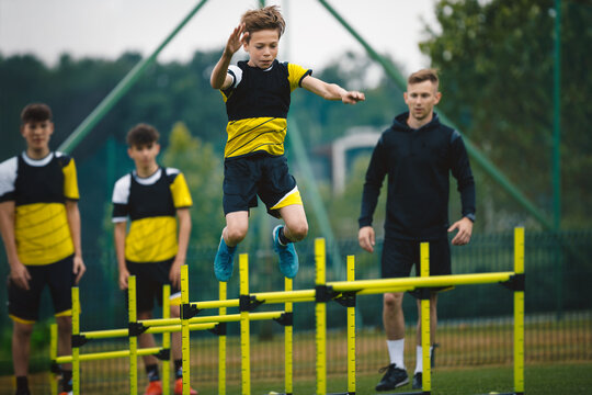 Teenage Boys in Soccer Training During Summer Camp. Boy Jumping High Over Hurdles. Players in Agility Training at Soccer Camp. Coach With Soccer Players at the Practice Unit