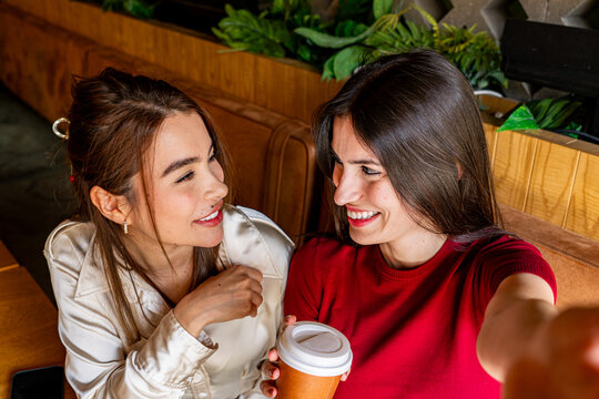 Two female friends are enjoying a coffee break together and capturing the moment with a selfie
