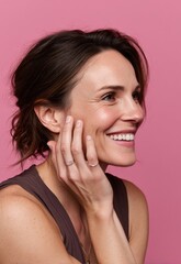Fototapeta premium In a vertical shot, a pretty girl with a natural makeup look is seen standing naked in front of a pink background, laughing and touching her clean skin after applying facial toners and serum