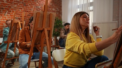 Group of adult people sitting at easels drawing pictures with pencils during master class in studio.