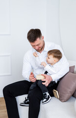 Fototapeta premium Dad and child having fun!. A father sits on a couch, engaging playfully with his young son who is holding a toy.