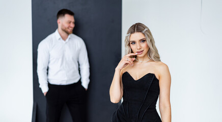 Couple in modern studio pose. A woman in a black dress poses confidently in front of a man wearing a white shirt in a unique studio environment.