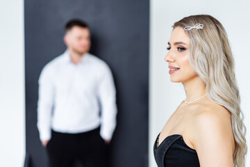 Stylish indoor couple photoshoot. A woman with long hair poses confidently, while a man stands in the background, creating a modern, elegant atmosphere.