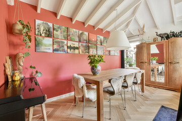 A modern dining room featuring a wooden table, eclectic artwork on a red wall, and vibrant floral arrangements, creating a cozy and artistic atmosphere.
