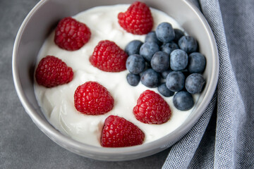 Gray bowl and natural yogurt with berries on the stone background.