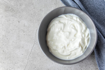 Gray bowl with white natural yogurt on the stone marble table.