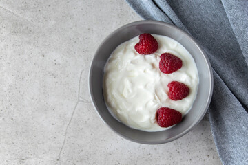 Gray bowl and natural yogurt with berries on the stone marble table.