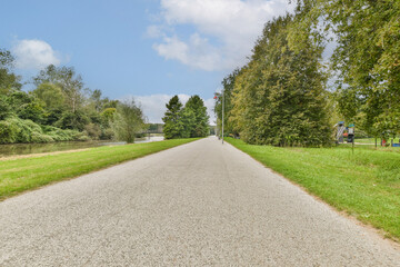 A picturesque pathway lined with trees leads alongside a serene waterway, creating a tranquil and inviting atmosphere perfect for leisure walks.