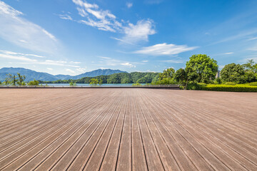 Empty wooden floor platform over lake and mountain landscape with blue sky and cloud background.