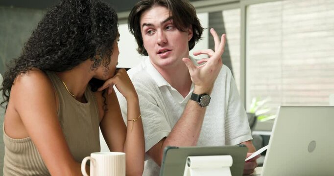 Happy diverse couple sitting at table, using laptop and smartphone, looking at documents