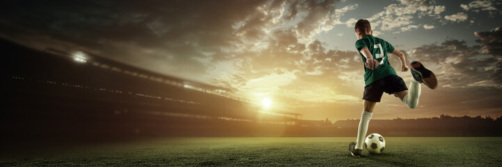 Back view of boy in green jersey runs into powerful kick at sunset on glowing soccer field. 3D...