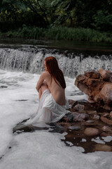 Aesthetic photo of attractive young woman in white translucent dress on river in image of nymph or mermaid