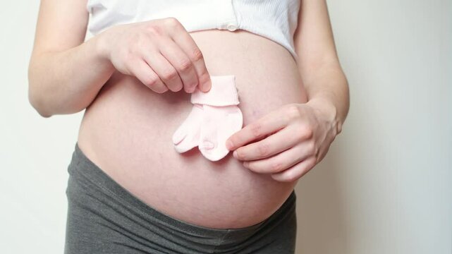 tiny baby socks against the background of a pregnant belly, pink socks