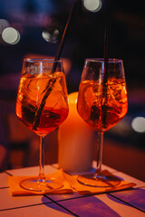 Two cocktail glasses with orange drink and straws on table in low light. Cocktail glow enhances nightlife, celebration, date vibe, cozy evening gathering outdoors
