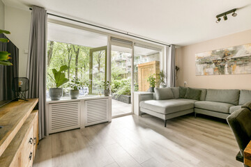 A stylish indoor lounge featuring large windows that let in plenty of natural light, complemented by greenery and modern furniture for a cozy atmosphere.